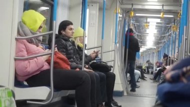 Moskova, Rusya - 21 Kasım 2019: Metro tren taşımacılığı. Sıcak giysili insanlar yeraltı vagonlarında oturuyorlar ve akıllı telefonlar kullanıyorlar. Bir erkek oturup bir şey düşünür, kız ve kadın.