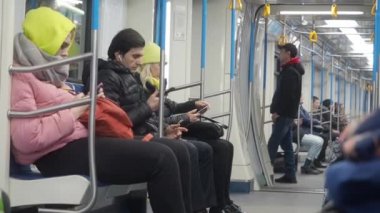 Moskova, Rusya - 21 Kasım 2019: Metro tren taşımacılığı. Sıcak giysili insanlar yeraltı vagonunda oturup alet kullanıyorlar. İnsanlar akıllı telefondan ücretsiz wi-fi internette geziniyor ya da e-posta okuyor.