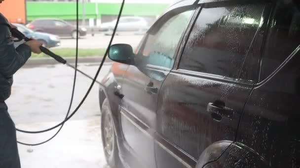 Мужчина моет черную машину. Slow Motion Video of a Car Washing Process on a Self-Service Car Wash. A Jet of Water with a High Pressure Wash Off the Dirt From the Car. Вид сбоку. Пенополистирол — стоковое видео