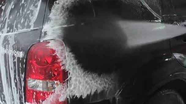 A man washes a black car. Slow Motion Video of a Car Washing Process on a Self-Service Car Wash. A Jet of Water With a High Pressure Wash Off the Dirt From the Car. Side View. Foamed Detergent Drains — 비디오