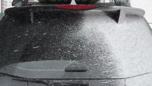 Διαδικασία πλύσης αυτοκινήτων σε ένα αυτοεξυπηρετούμενο πλυντήριο αυτοκινήτων.Ένα αεριωθούμενο νερό με ένα πλύσιμο υψηλής πίεσης από τον αφρό από το πίσω παράθυρο του αυτοκινήτου. Ένας άνδρας πλένει ένα μαύρο αυτοκίνητο Καλύπτει το γυαλί του αυτοκινήτου με σαπουνόφουσκες — Αρχείο Βίντεο
