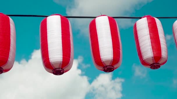 Oosters papier rood-witte lantaarns Chochin opknoping op witte bewolkte blauwe lucht achtergrond. Japanse lantaarns hangen op een heldere hemelse achtergrond. Pan rechts — Stockvideo