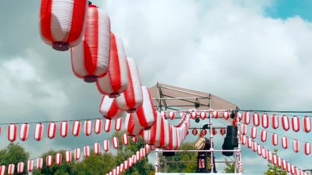 Il palco dello Yagura con un grande tamburo taiko giapponese Odaiko. Molte lanterne bianco-rosse di carta Chochin oscillavano nel vento su sfondo bianco di nuvole. Paesaggio per la vacanza Obon quando la gente balla di — Video Stock