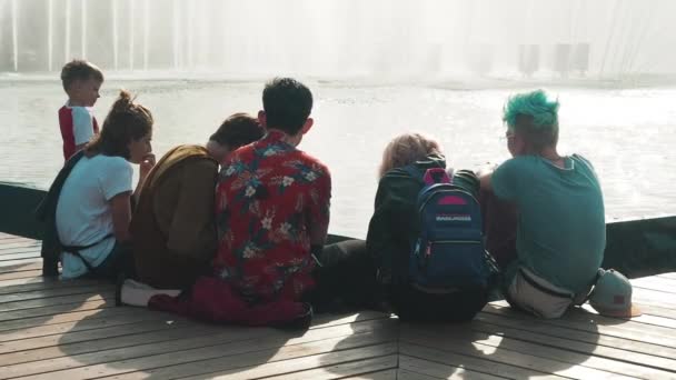 Moskou, Rusland - 21 juli 2019: Vrienden communiceren buiten. De jeugd zit bij de fontein. Tieners chillen bij het water in het park. Een groep tieners die samen ergens over praten. — Stockvideo