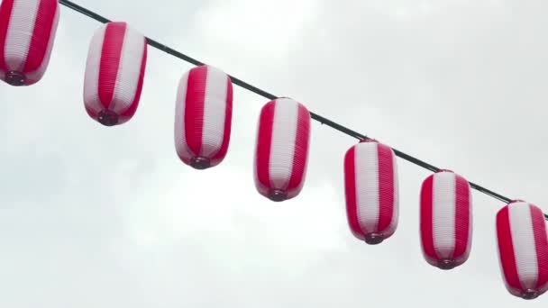 Oosters papier rood-witte lantaarns Chochin opknoping op sombere bewolkte hemel achtergrond. Japanse lantaarns opknoping op lucht achtergrond. — Stockvideo