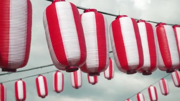 Veel oosters papier rood-witte lantaarns Chochin opknoping op witte bewolkte blauwe lucht achtergrond. Japanse lantaarns opknoping op heldere hemel achtergrond — Stockvideo