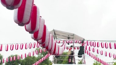Yagura sahnesinde büyük bir Japon Taiko davulu Odaiko. Birçok kağıt kırmızı-beyaz fener Chochin rüzgarda sallanıyor beyaz bulutların arkasında. İnsanların dans ettiği bayram manzarası.