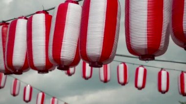 Many oriental paper red-white lanterns Chochin hanging on white cloudy blue sky background. Japanese lanterns hanging on bright sky background