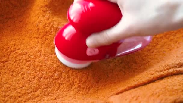 Clothes care. Lint shaver or fabric shaver or fuzz remover in female hand. Woman removing lint on orange wool coat with handheld electric defuzzer — Stok video