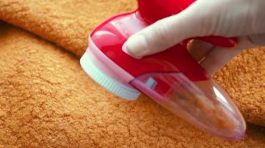 Clothes care. Lint shaver or fabric shaver or fuzz remover in female hand. Woman removing lint on orange wool coat with handheld electric defuzzer