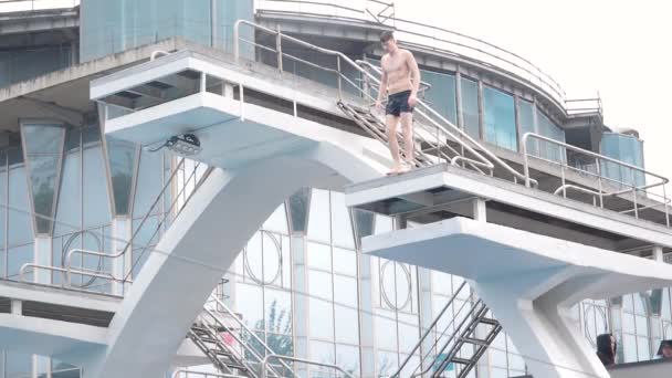 Moskau, Russland - 12. Oktober 2019: Ein junger Mann springt aus großer Höhe von einem Sprungturm in ein Freibad. Es regnet leicht und es ist kalt. Ein wettbewerbsfähiger Sprungturm am — Stockvideo