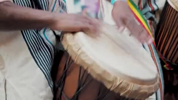 Afričtí bubeníci v etnickém oblečení hrají na buben djembe zblízka. Hudebník tluče rytmus na afrických bubnech. Černí umělci buší do bubnů rukama — Stock video
