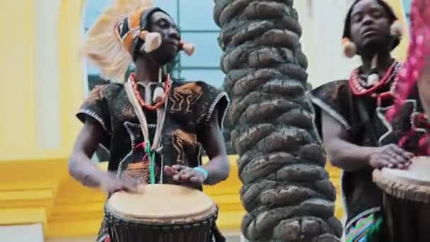 MOSCOW, RÚSSIA- FEVEREIRO 29, 2020: Bateristas africanos em roupas étnicas tocando no tambor djembe. Músico bate ritmo em tambores africanos. Artistas negros batem na bateria com as mãos. Meninas dançarinas dança — Vídeo de Stock