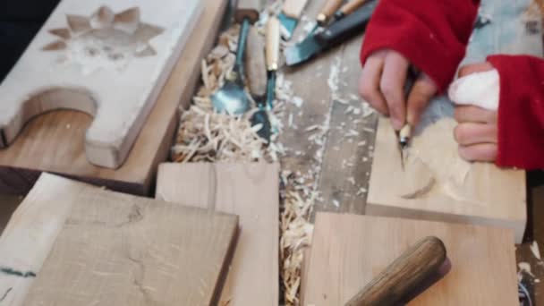 Un artesano talló un plato para hornear pan de jengibre y galletas de madera con un cuchillo. Arte tallador de madera hace tallas de madera. Detalle de las manos trabajadoras. El escultor hace la escultura. Artesanía tradicional — Vídeo de stock