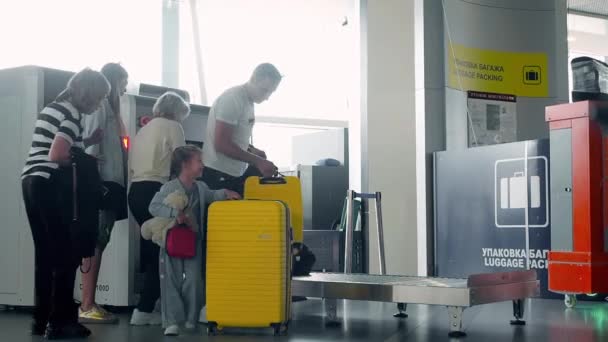 Pyatigorsk, Ryssland - 11 september 2019: Glad familj hämtar gula resväskor från skannern på flygplatsen. Bagaget passerar genom röntgenskannrar vid säkerhetskontrollen i säkrade områden — Stockvideo