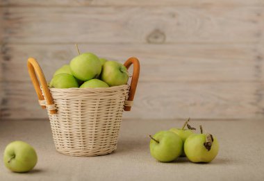 Hafif ahşap bir arka plan üzerinde bir hasır sepet içinde yeşil elma.