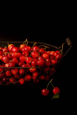 Siyah bir arka plan üzerinde metal bir sepet içinde kiraz. 