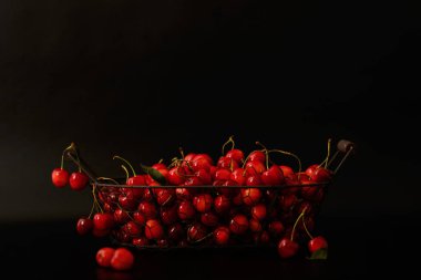 Siyah bir arka plan üzerinde metal bir sepet içinde kiraz. 