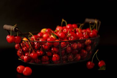 Siyah bir arka plan üzerinde metal bir sepet içinde kiraz. 