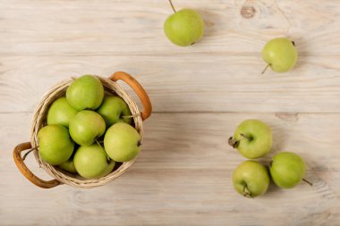 Hafif ahşap bir arka plan üzerinde bir hasır sepet içinde yeşil elma. 
