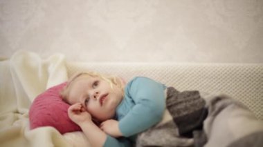 Küçük sevimli komik çocuk (3 yaşında, sarışın) ekose bir kanepenin altında uzanıyor ve TV 'de çizgi film izliyor.