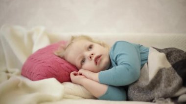 Küçük sevimli komik çocuk (3 yaşında, sarışın) ekose bir kanepenin altında uzanıyor ve TV 'de çizgi film izliyor.