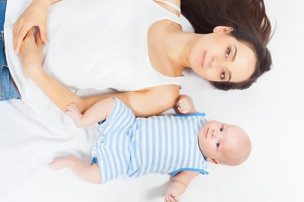 Bebé feliz tendido cerca de su madre en una cama blanca —  Fotos de Stock
