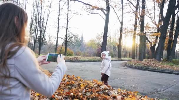 Mãe faz filmagens de bebê no parque de outono, telefone celular — Vídeo de Stock