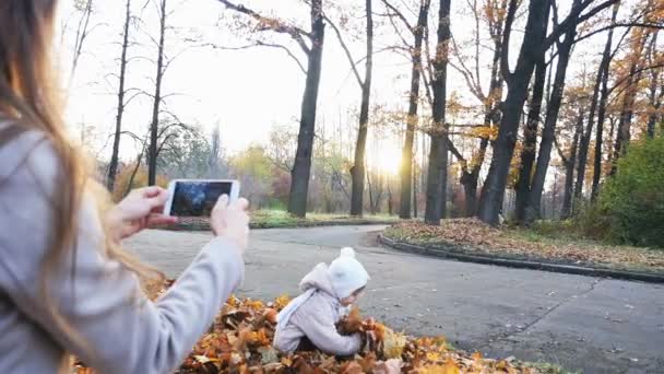 Madre hace imágenes del bebé en el parque de otoño, teléfono móvil — Vídeo de stock