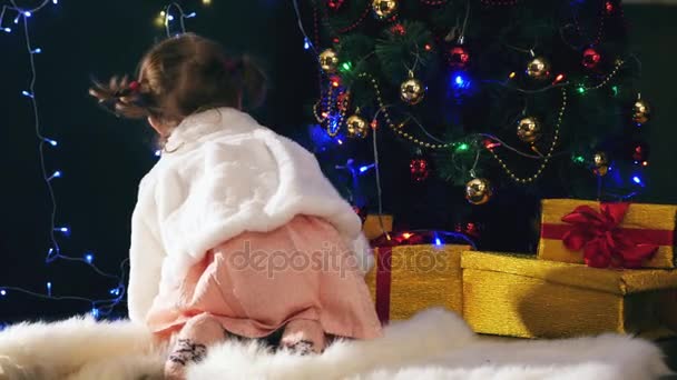 Menina abre caixas de presentes de Natal perto da lareira, árvore Cristmas decorado — Vídeo de Stock