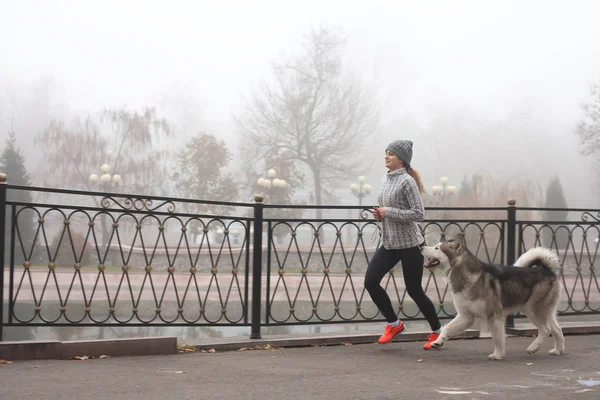 Image of young girl running with her dog, alaskan malamute — Stock Photo, Image