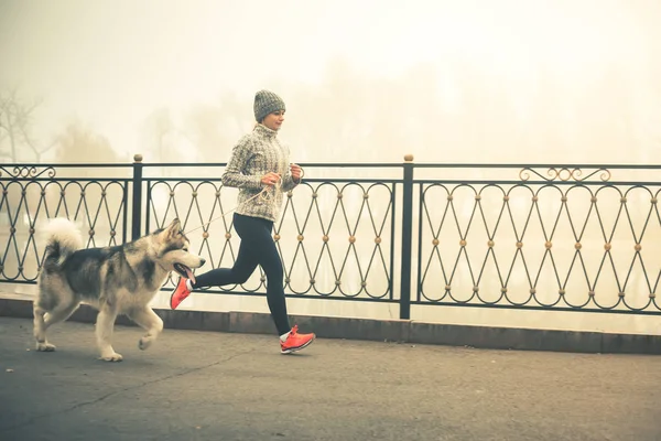 Изображение молодой девушки, бегущей со своей собакой, аляскинский маламут — стоковое фото