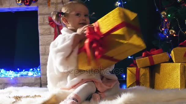 Menina abre caixas de presentes de Natal perto da lareira, árvore Cristmas decorado — Vídeo de Stock