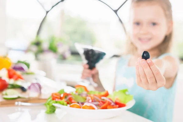 Närbild Söt liten flicka gör sallad. Holding oliv. Barn matlagning. — Stockfoto