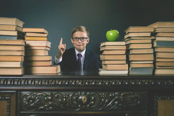 Intelligens iskola fiú ül az asztal, a sok könyv — Stock Fotó