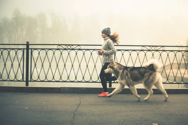 Imagen de una jovencita corriendo con su perro, Alaska Malamute —  Fotos de Stock