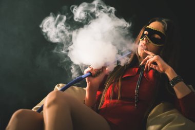 Genç, güzel kız karnaval maskesi olan bir nargile duman