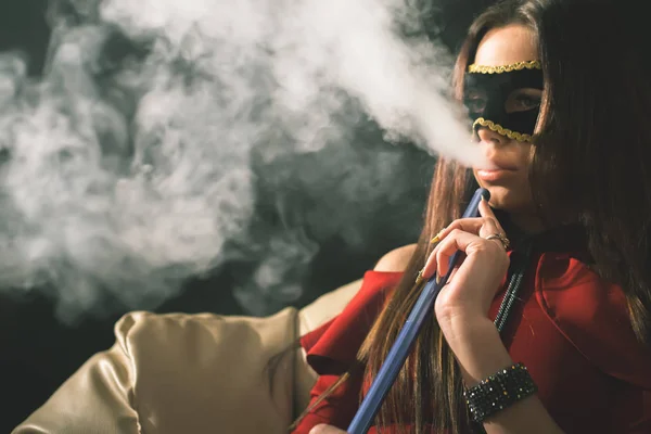 Jovem, menina bonita com máscara de carnaval fumar um narguilé — Fotografia de Stock