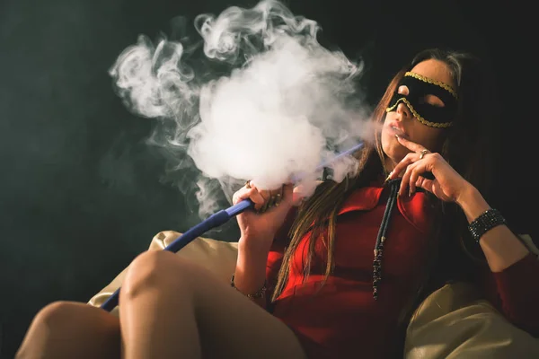 Jovem, menina bonita com máscara de carnaval fumar um narguilé — Fotografia de Stock