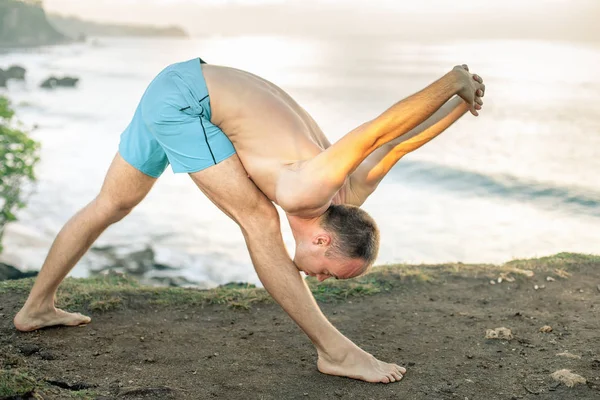 Bello uomo che fa yoga a scogliera con sfondo blu del mare — Foto Stock