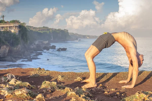Cliff mavi deniz arka plan ile Yoga yapan yakışıklı erkek