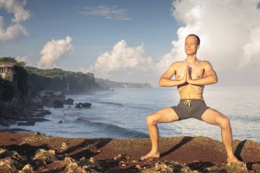 Cliff mavi deniz arka plan ile Yoga yapan yakışıklı erkek