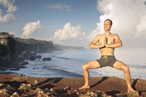 Cliff mavi deniz arka plan ile Yoga yapan yakışıklı erkek