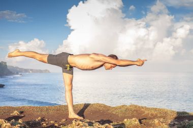 Cliff mavi deniz arka plan ile Yoga yapan yakışıklı erkek