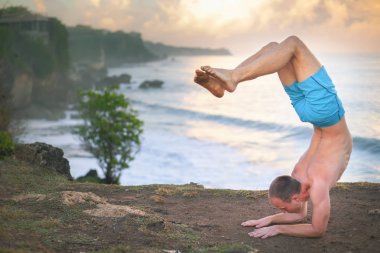 Cliff mavi deniz arka plan ile Yoga yapan yakışıklı erkek