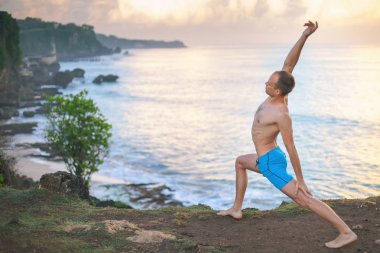 Cliff mavi deniz arka plan ile Yoga yapan yakışıklı erkek