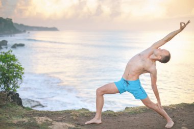 Cliff mavi deniz arka plan ile Yoga yapan yakışıklı erkek