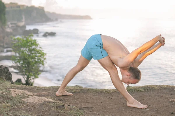 Cliff mavi deniz arka plan ile Yoga yapan yakışıklı erkek