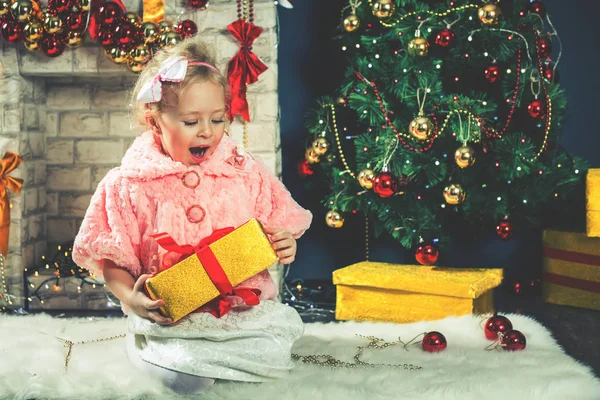 Divertente bambina apre la scatola regalo di Natale vicino all'albero di Natale — Foto Stock