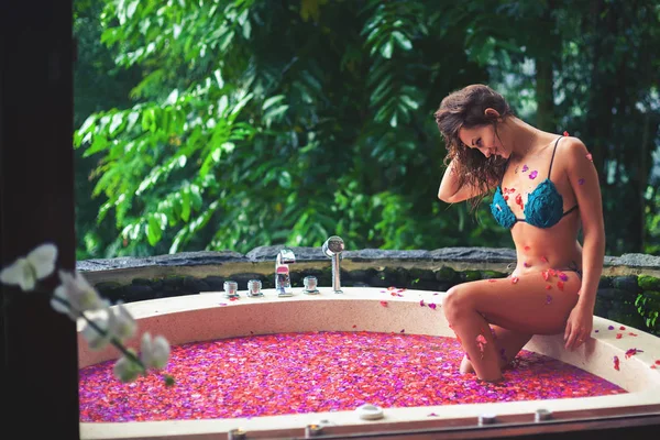 Vrouw ontspannen bad met tropische bloemen buiten in luxehotel — Stockfoto
